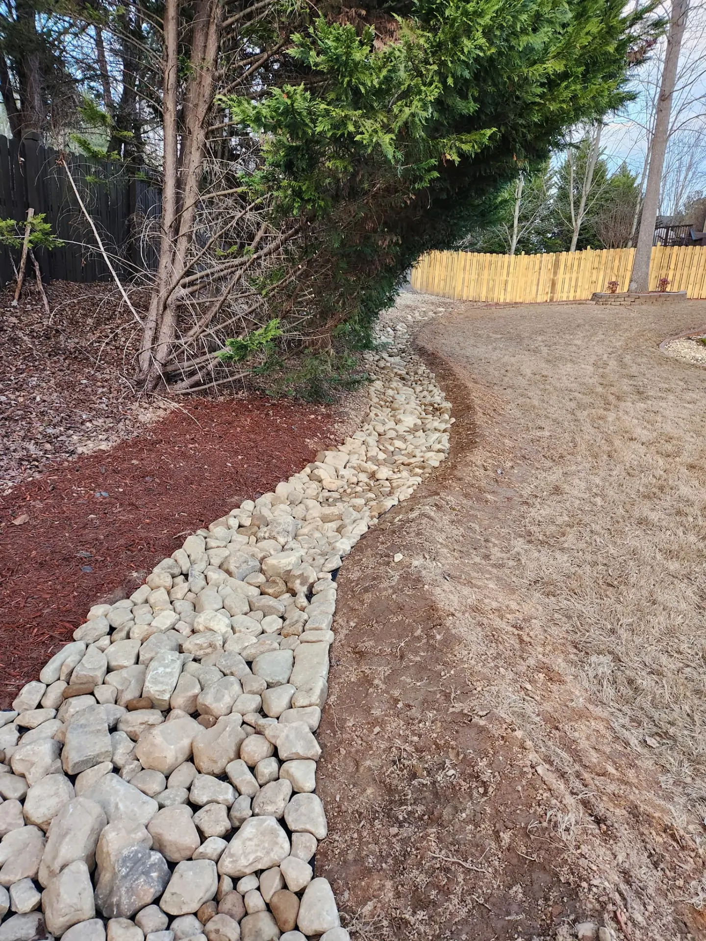 Curved river rock drainage channel bordered by fresh mulch