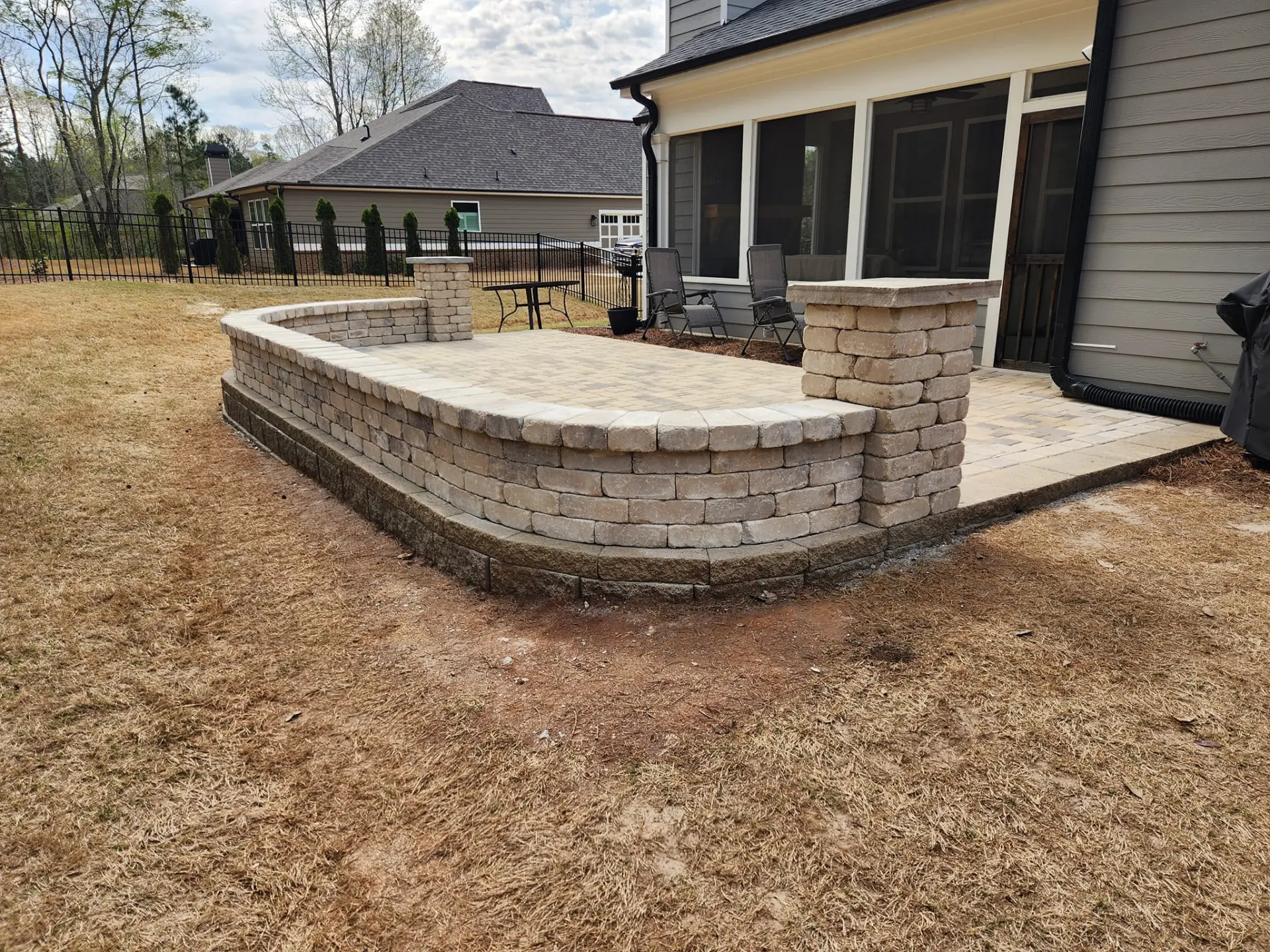 Wide view of a raised paver patio with a curved seating wall