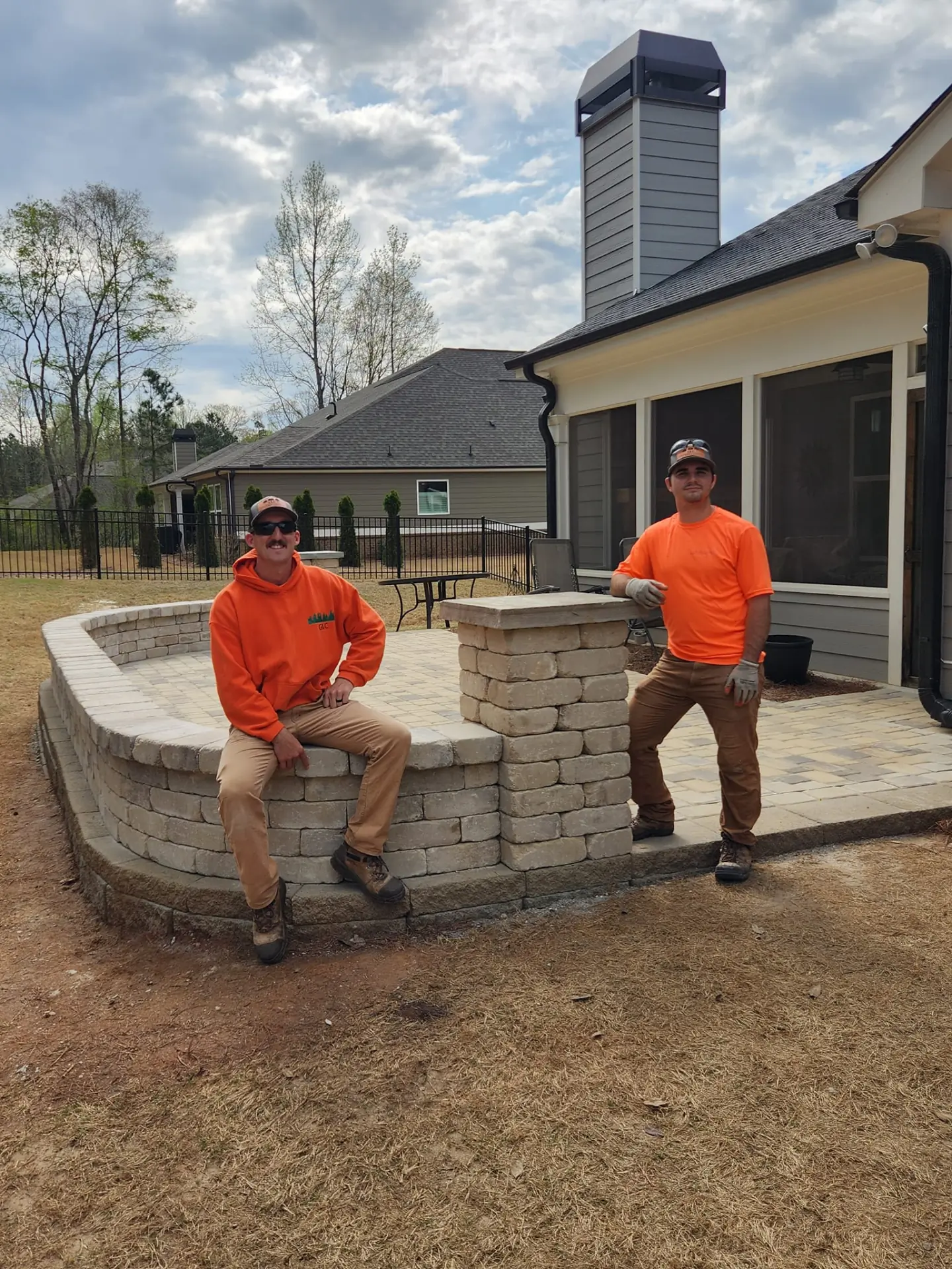 Two landscapers seated on the completed wall of a new backyard patio