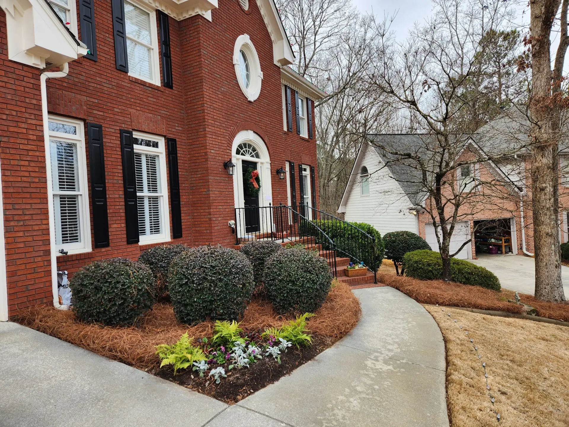 Fresh pine straw surrounding trimmed shrubs and seasonal flowers