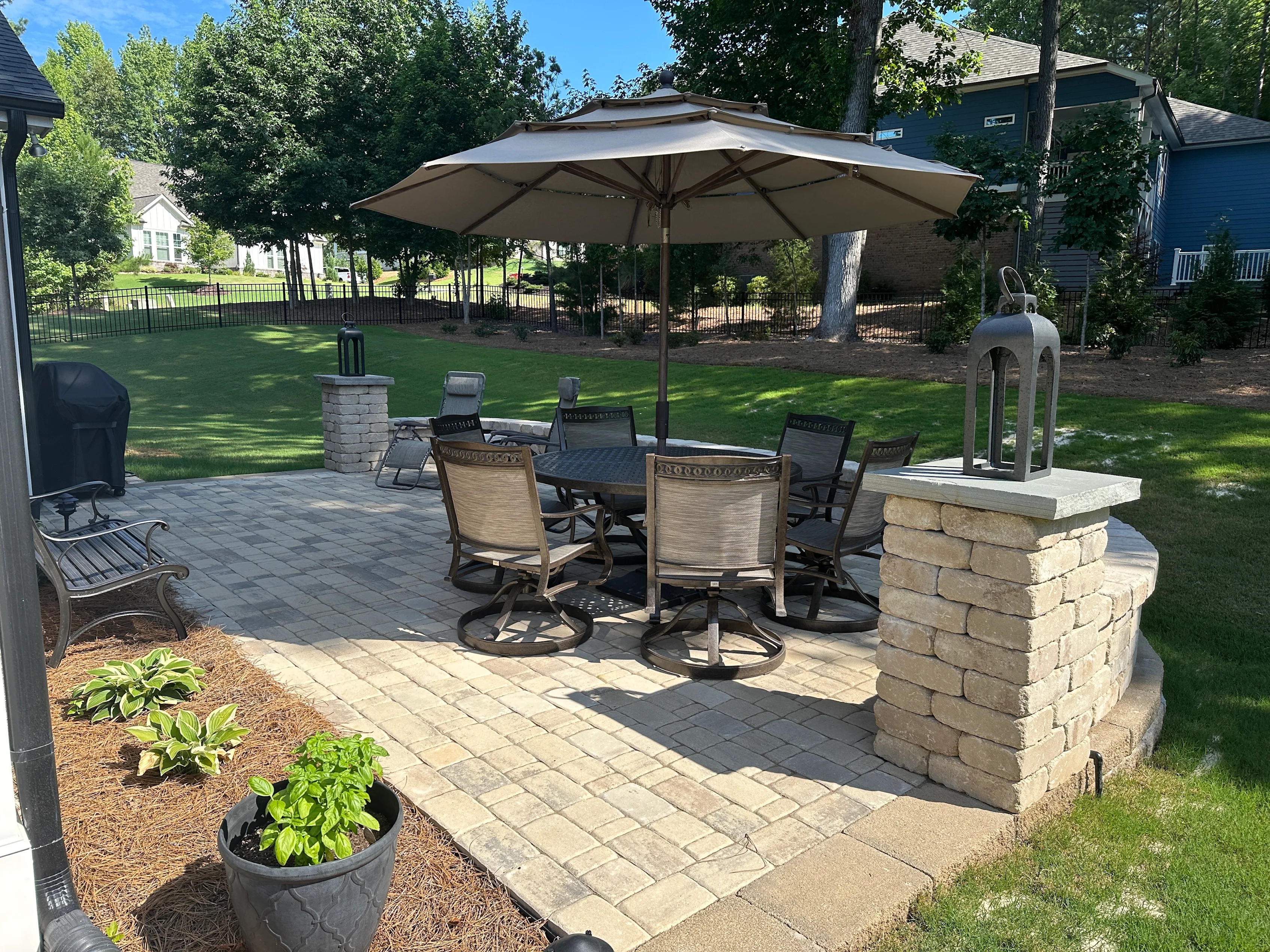 Furnished backyard paver patio with a seating wall and stone columns
